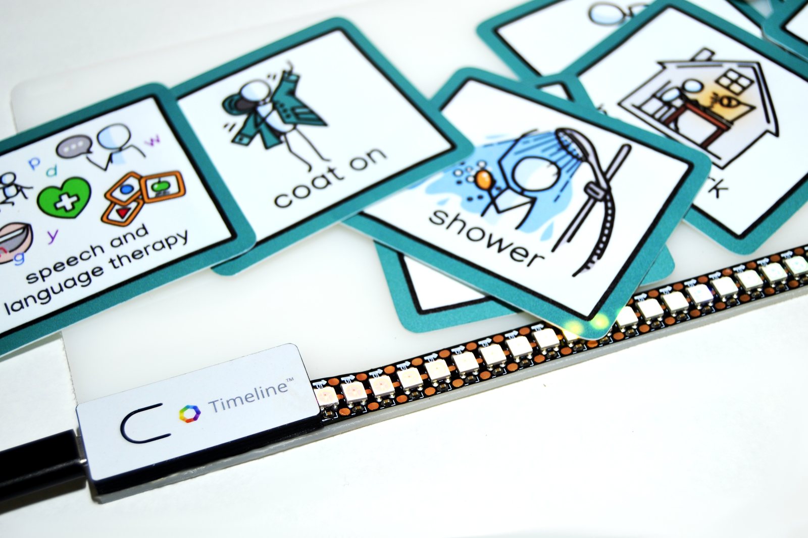 The Timeline control unit and lit LED strip beside daily-routine picture cards - speech and language therapy, coat on, shower